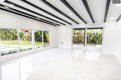 A spacious room with white walls and floor, large windows, and a ceiling with black and white stripes.