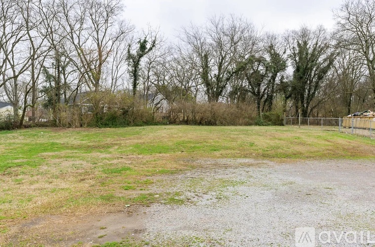 A grassy field with a fence and trees in the background.