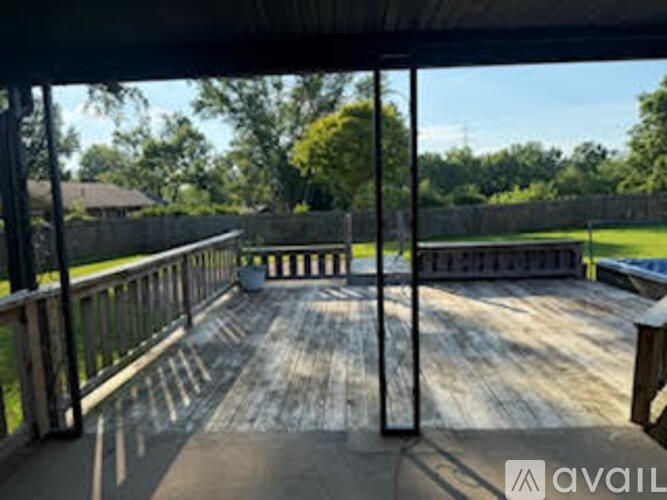 A wooden deck with a railing and a view of a grassy area and trees.