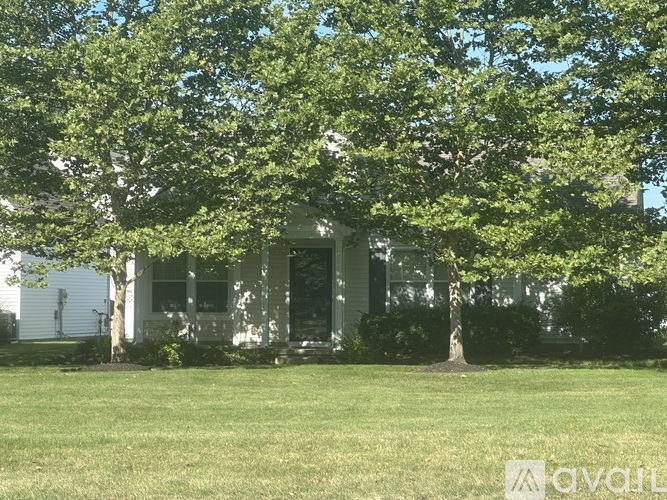 A white house with a black door and windows is surrounded by green trees.