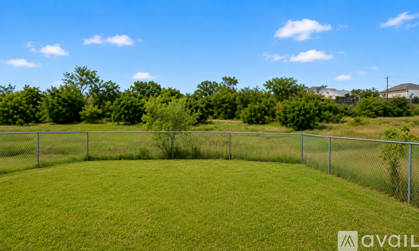 A grassy field with a fence and trees in the background.