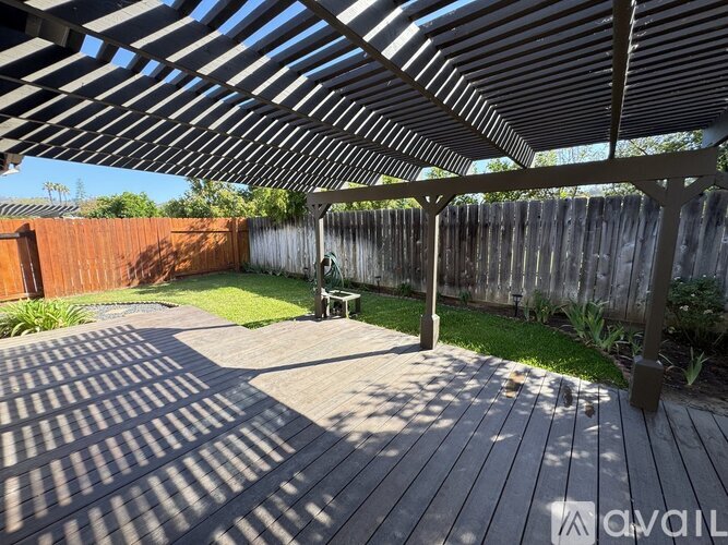 A wooden deck with a pergola and a bench in the middle of a backyard.