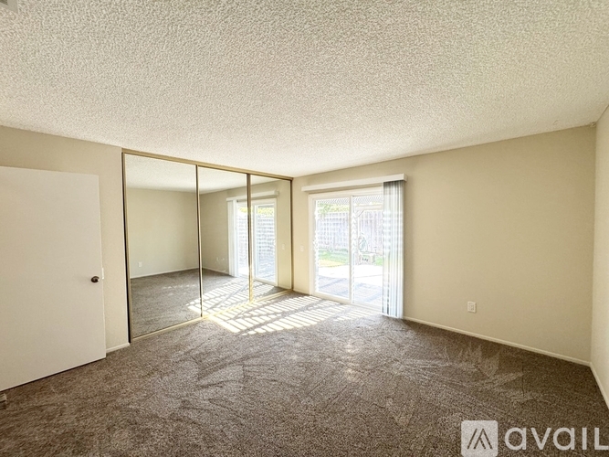 A spacious room with a carpeted floor and sliding glass doors leading to a balcony.