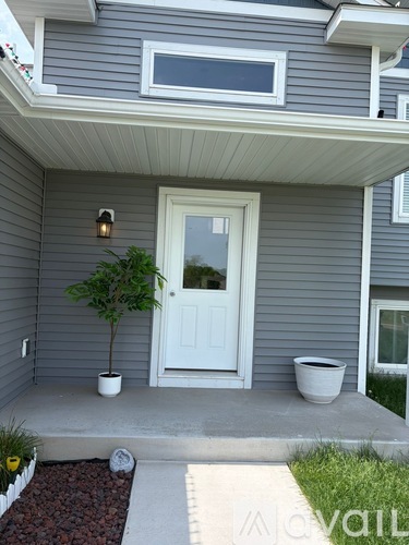 A grey house with a white door and a small tree in a white pot.
