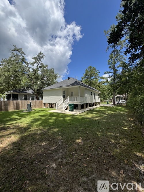 A white house with a grey roof is surrounded by a green lawn and trees.