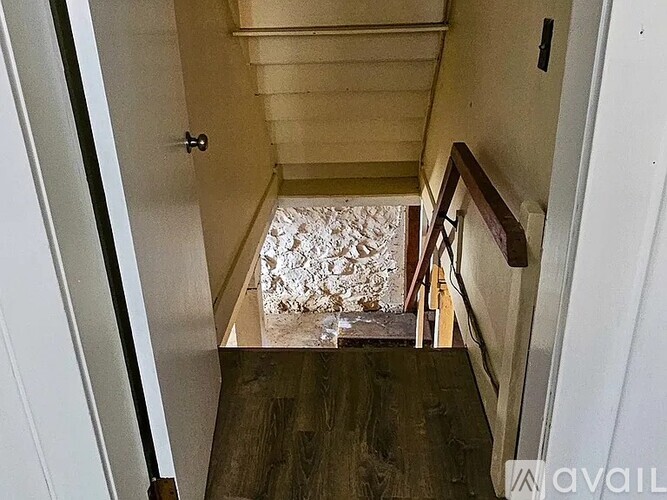 A hallway with a wooden floor and a staircase leading to a bedroom.