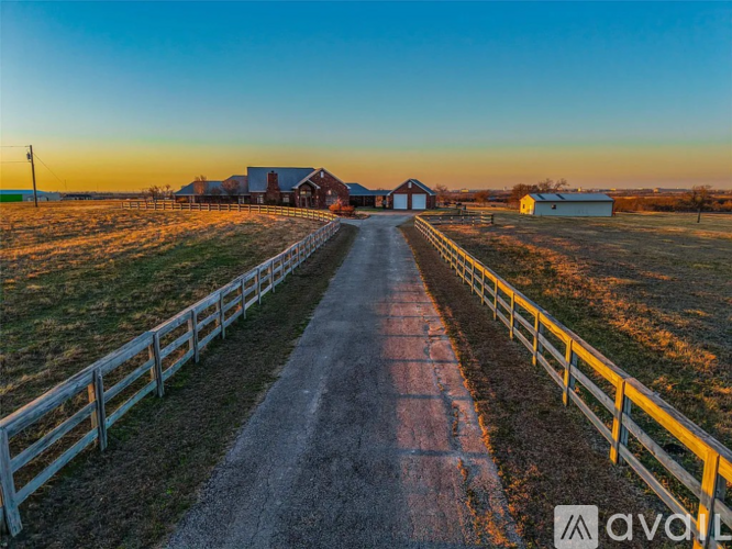 A long, narrow road with a white fence on both sides leads to a red barn.