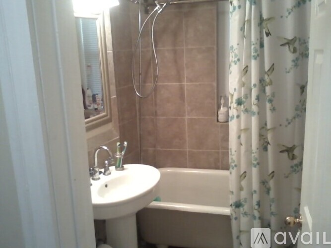 A small white sink is in a bathroom with a shower curtain and a tub.