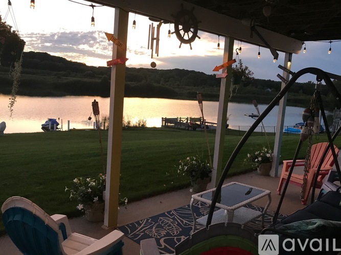 A patio with chairs and a table overlooking a lake at sunset.