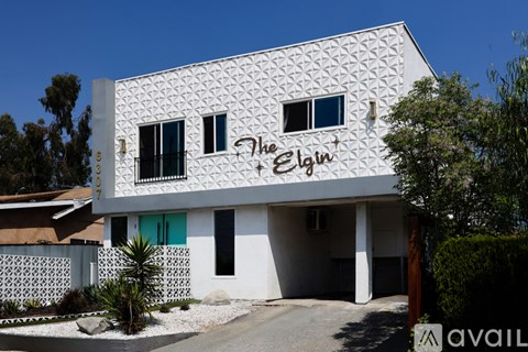 A white building with a black fence and a sign that says "The Elgin".