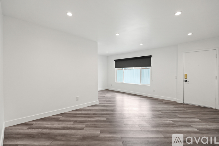 A spacious room with wooden flooring and a window with blinds.
