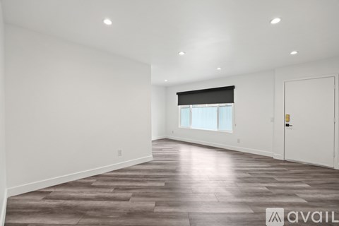 A spacious room with wooden flooring and a window with blinds.