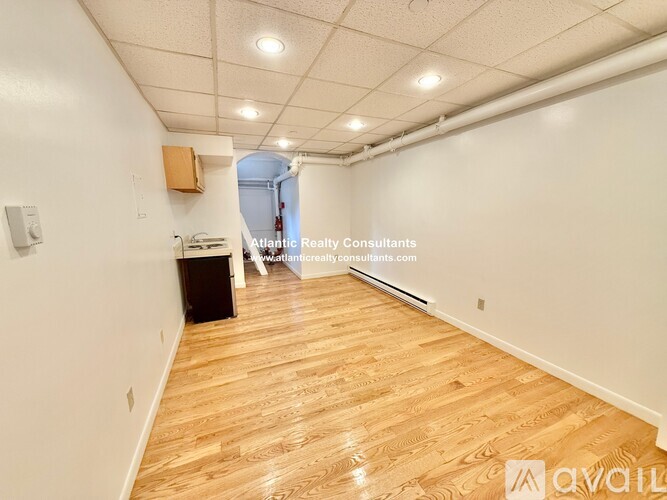 A room with wooden flooring and white walls, with a door in the background.