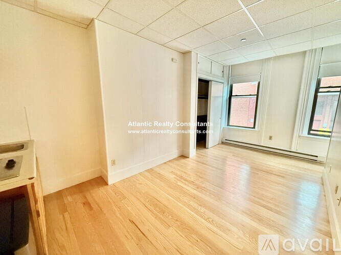 A spacious room with wooden flooring and a window on the right side.