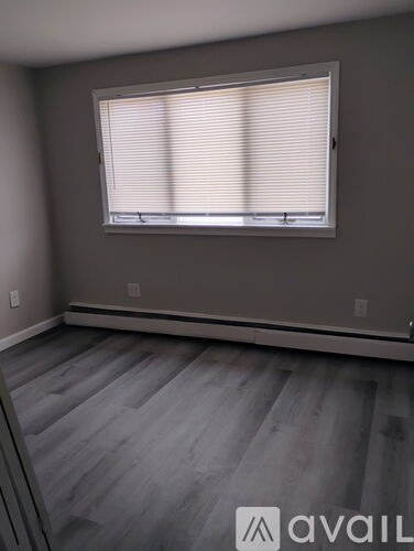 A room with a window covered in blinds and wooden flooring.