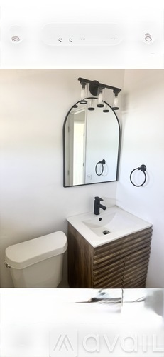 A bathroom with a white toilet and a wooden cabinet with a mirror above it.
