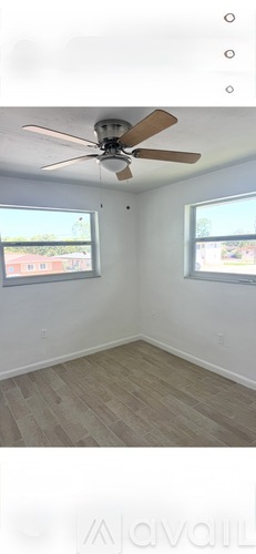 A room with a ceiling fan and two windows.