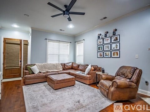 A living room with a brown leather couch and ottoman, a ceiling fan, and a wall with framed pictures.
