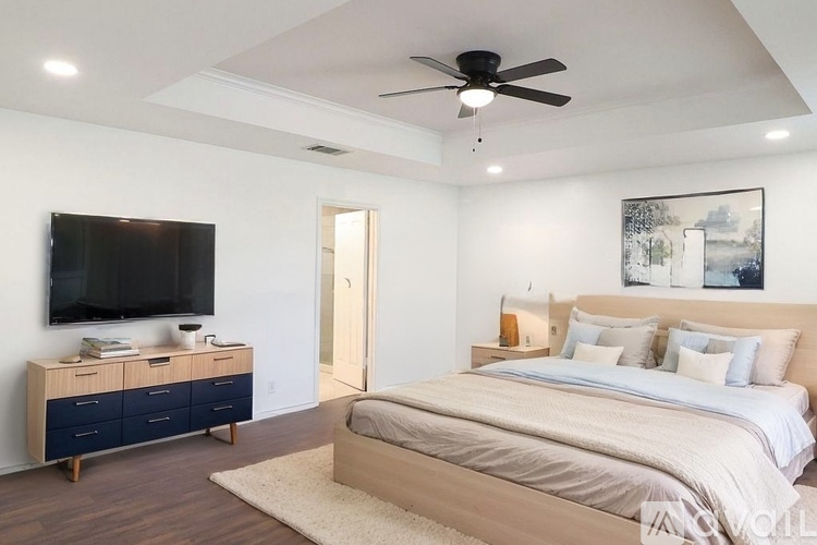 A bedroom with a bed, a television, and a ceiling fan.