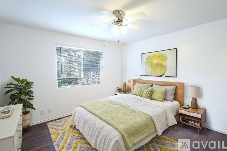A bedroom with a bed, a ceiling fan, and a window with a view of trees.