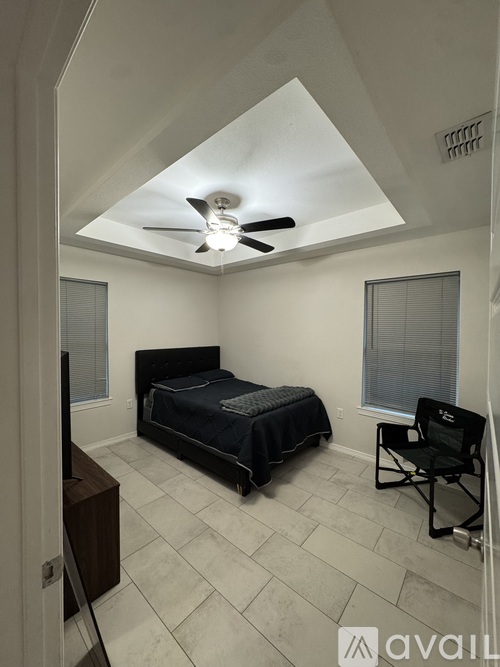 A bedroom with a bed, chair, and ceiling fan.