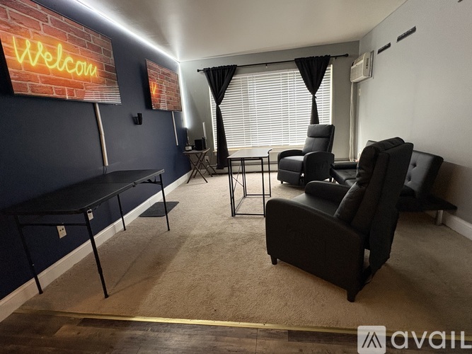 A room with a neon sign that says "Welcome" and two black leather chairs.