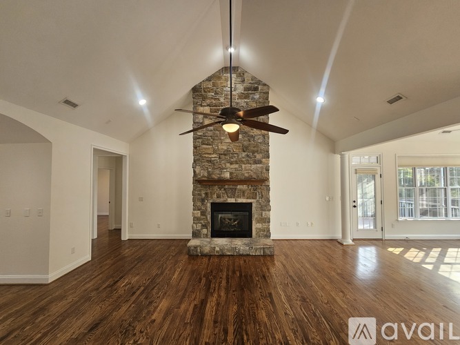 A spacious living room with a stone fireplace and hardwood floors.