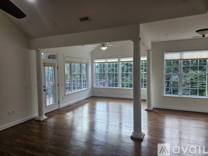 A spacious room with wooden floors and white columns.