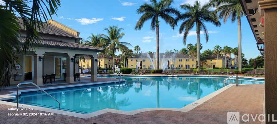 A pool surrounded by palm trees and a building with a patio.