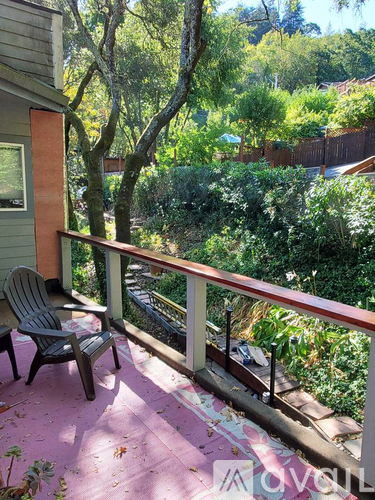 A balcony with a chair and a table is surrounded by greenery.
