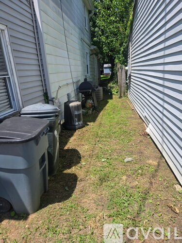 A grey trash can sits on a grassy area between two houses.