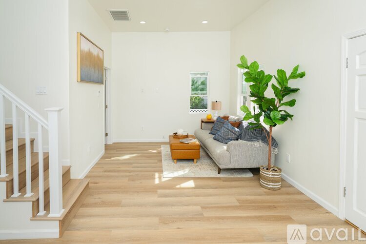 A living room with a couch, a potted plant, and a painting on the wall.