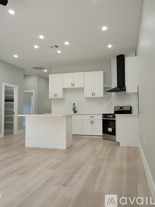 A modern kitchen with white cabinets and a wooden floor.