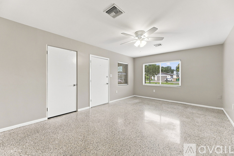 A spacious room with a ceiling fan and a large window showing a view of a building outside.