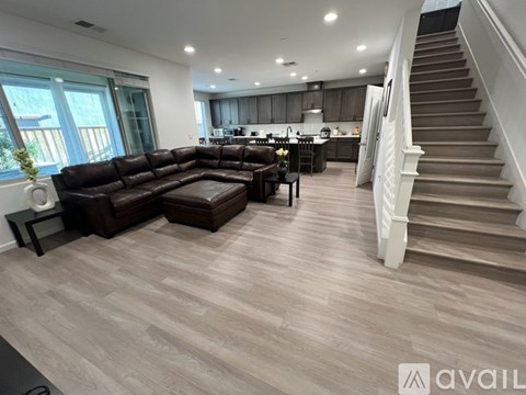 A spacious living room with a brown leather sofa and a staircase.