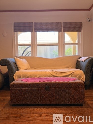 A brown ottoman with a pink blanket on top of it sits in front of a couch.