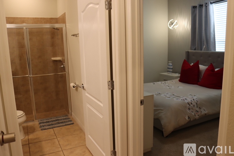 A bathroom with a walk-in shower and a bedroom with a bed and pillows.