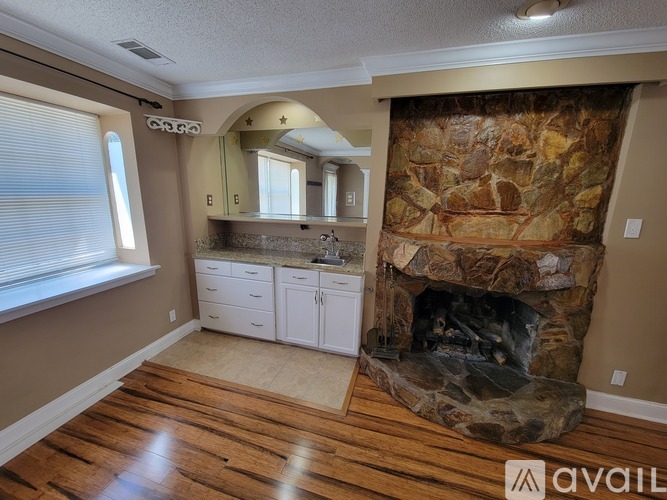 A stone fireplace is in the corner of a room with wood flooring.