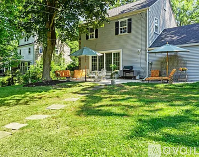 A house with a lawn and a patio with chairs and an umbrella.