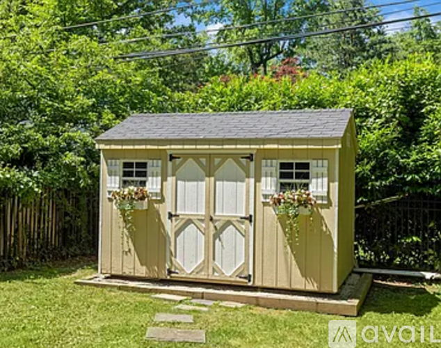 A small house with a brown roof and white trim is surrounded by greenery.