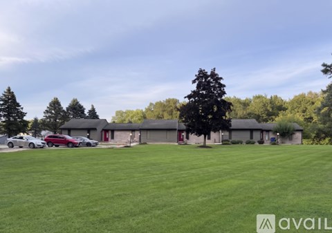A grassy field with a building and trees in the background.