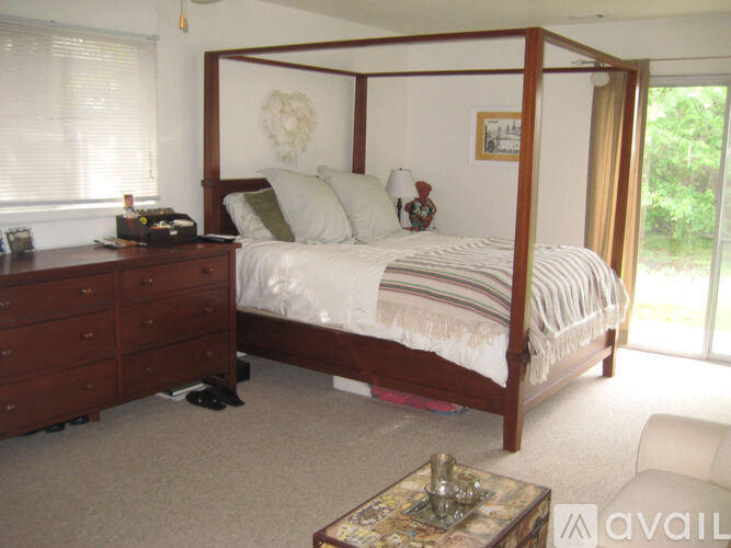 A bedroom with a four poster bed, a dresser and a table.