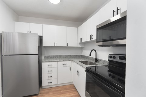 A modern kitchen with a stainless steel refrigerator and black countertops.