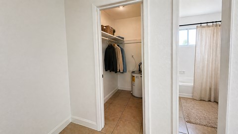 A white closet with clothes hanging and a trash can.