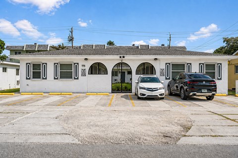 Two cars are parked in front of a white building with a yellow door.