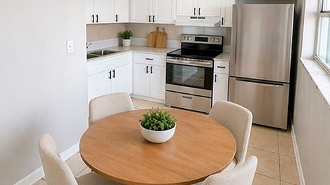 A kitchen with a table and chairs in the foreground and a refrigerator, oven, and cabinets in the background.