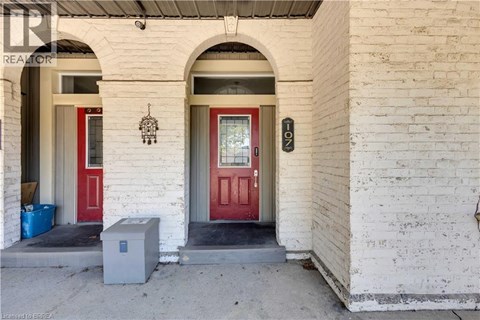 A white building with a red door and a small grey box in front.