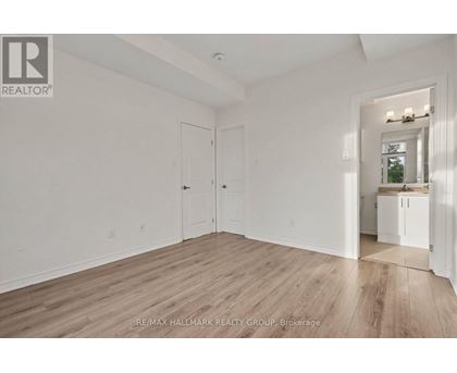 A spacious room with wood flooring and white walls, with a doorway leading to another room.