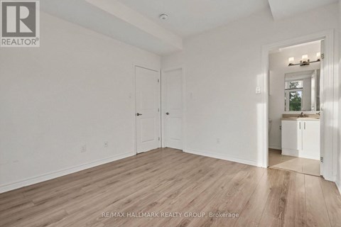 A spacious room with wood flooring and white walls, with a doorway leading to another room.