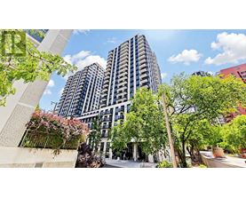 A modern building with a lot of windows and balconies is surrounded by trees and plants.
